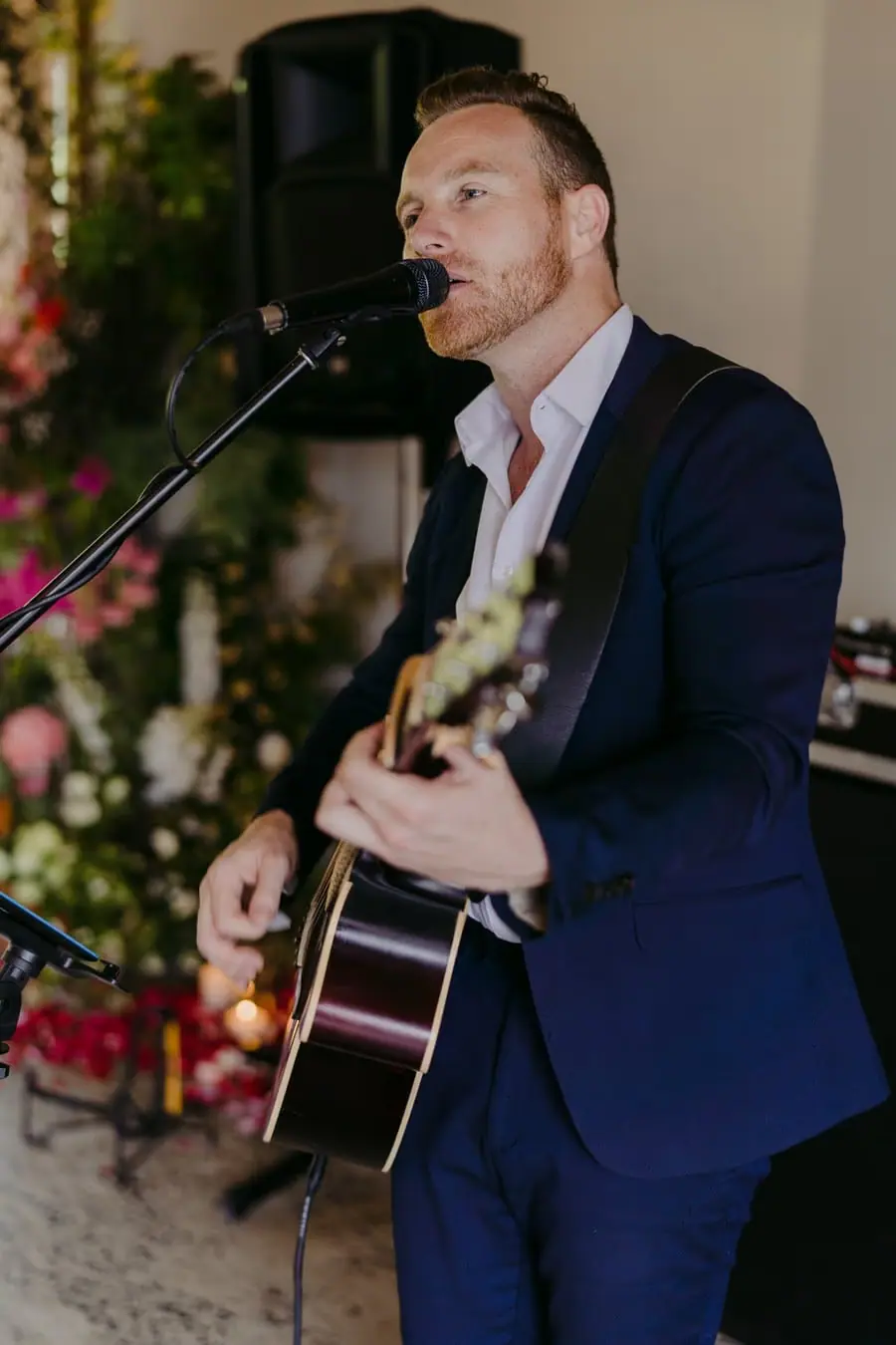 Musician playing guitar and singing into a microphone indoors.