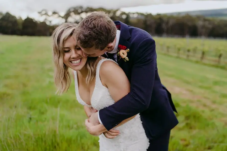 Groom embracing the bride from behind and leaning close to her face.