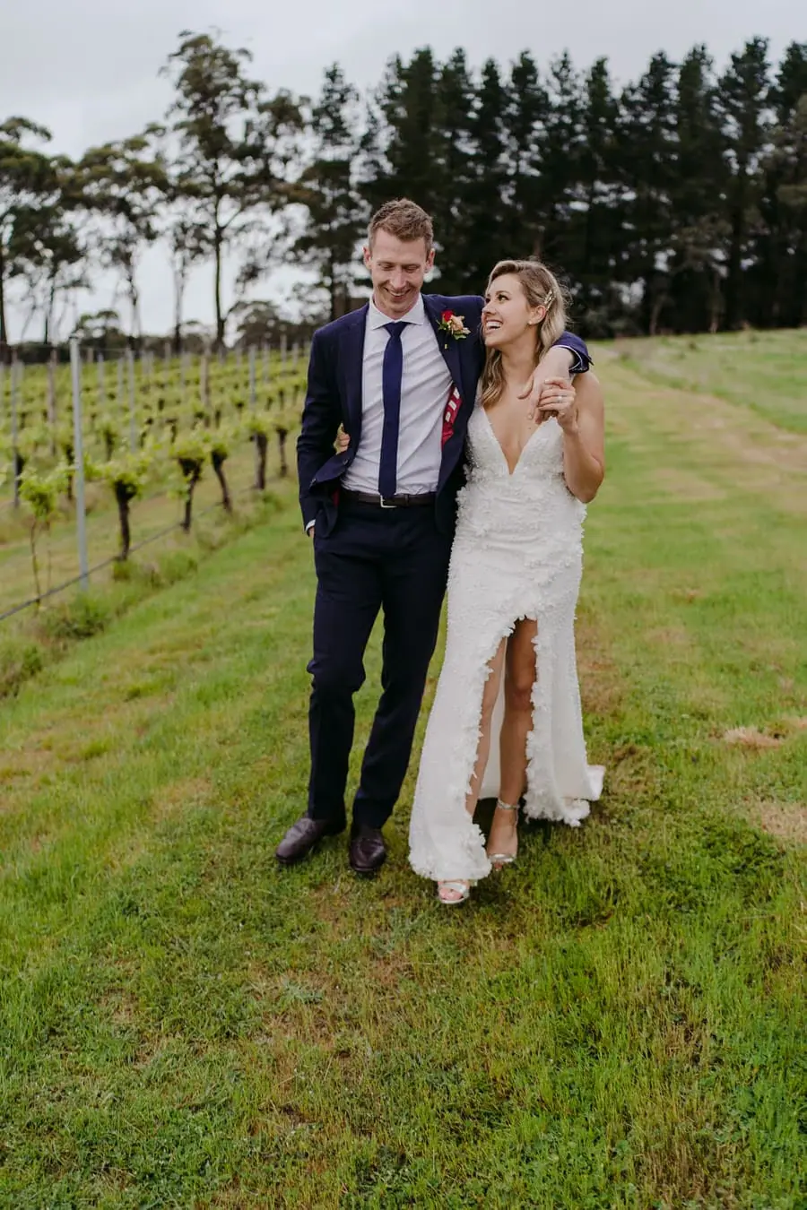 Couple walking arm in arm beside rows of grapevines.