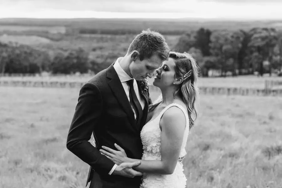 Black-and-white portrait of the couple embracing in a field.