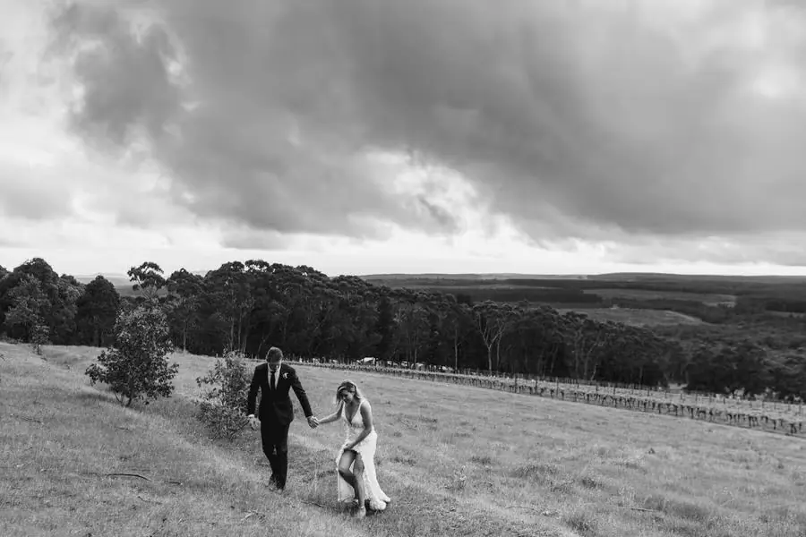 Black-and-white wide view of the couple walking uphill across a grassy field.