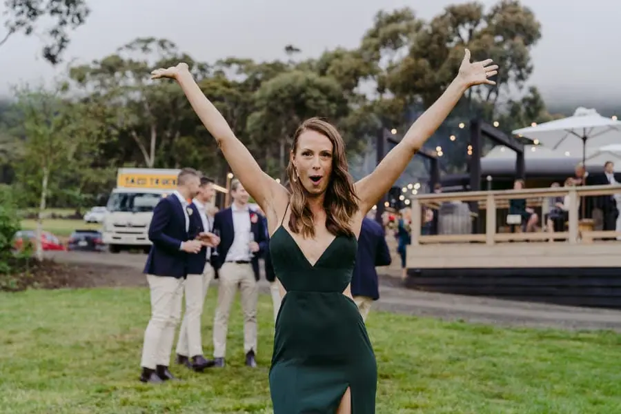 Woman in a dark green dress raising both arms on the lawn.