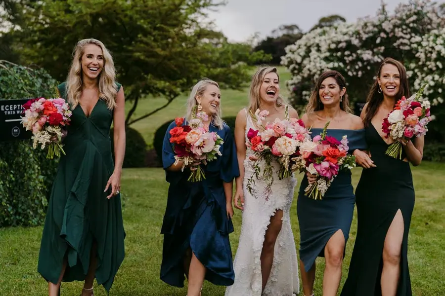 Bride and four women laughing together while holding pink and red bouquets.