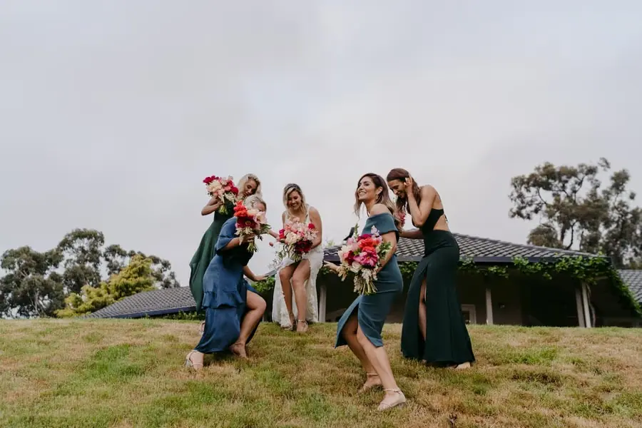 Bride and companions laughing as they walk down a grassy slope.