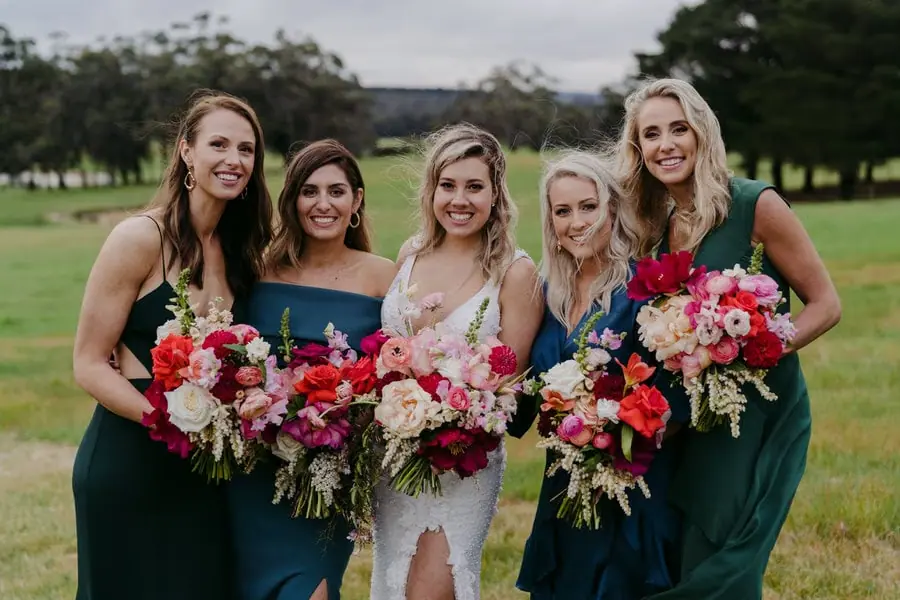 Bride and four women smiling together with colourful flower bouquets.