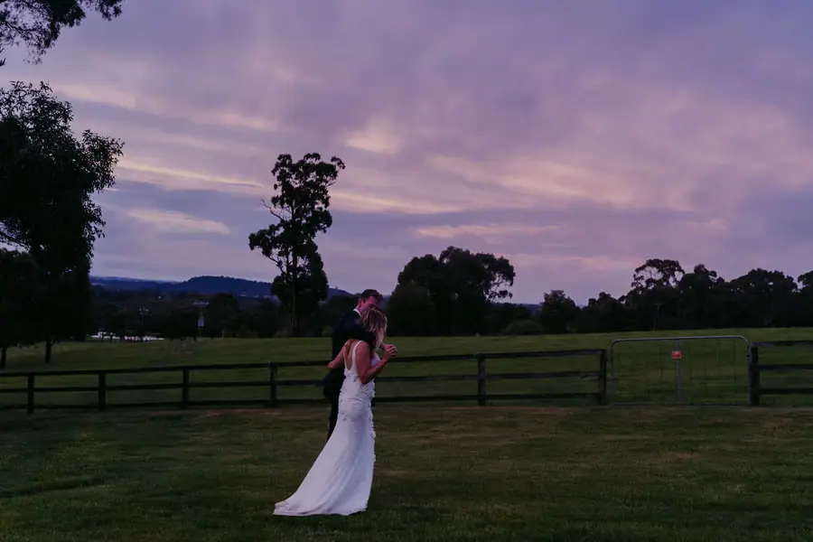 Bride raising her bouquet beneath a purple sunset sky.