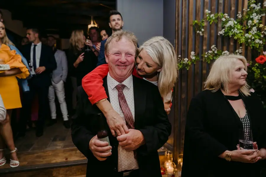 Woman in red embracing a smiling man from behind inside the reception.
