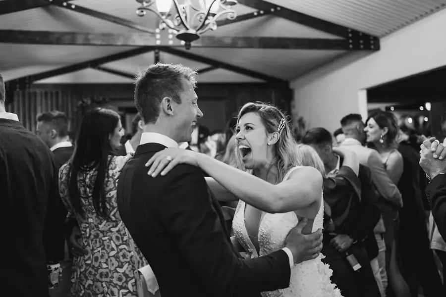 Black-and-white photograph of the bride and groom dancing among their guests.