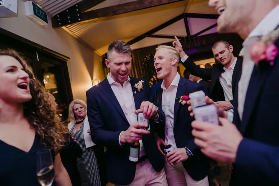 Men laughing and dancing together with drinks at the reception.