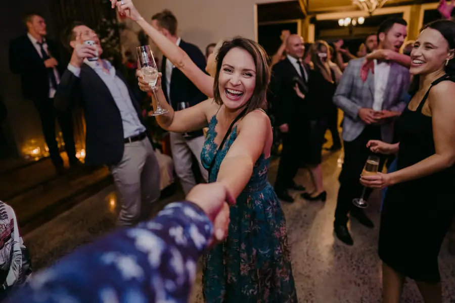 Woman in a patterned dress raising her drink and laughing on the dance floor.