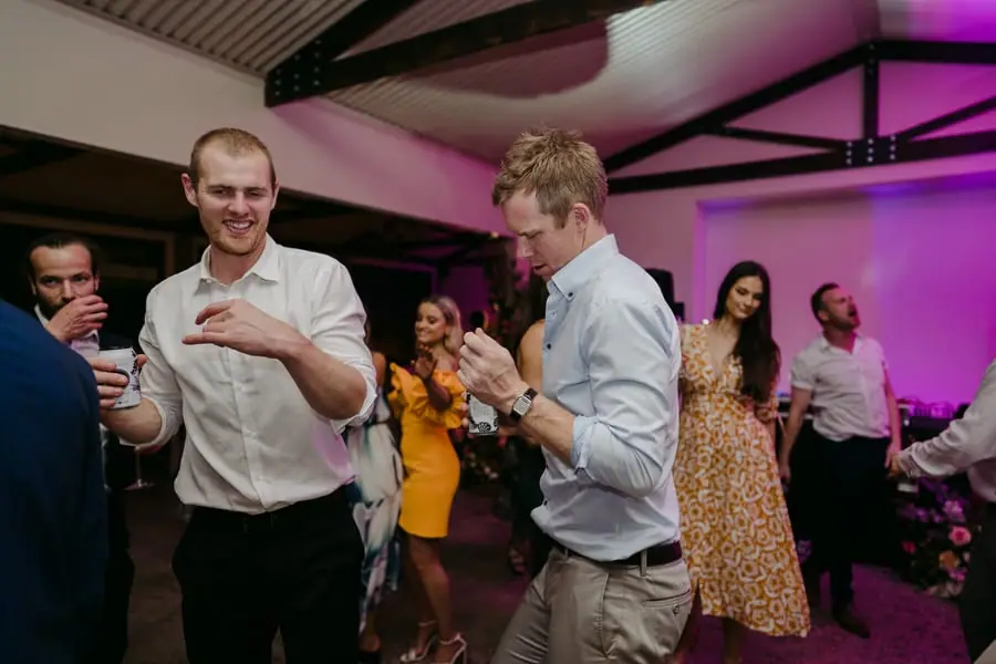 Two men dancing together under purple reception lighting.