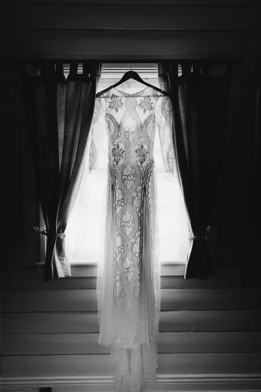 Black-and-white photograph of a lace wedding dress hanging in a window
