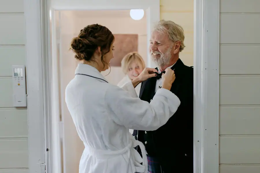 Bride in a dressing gown adjusting a smiling older man’s bow tie