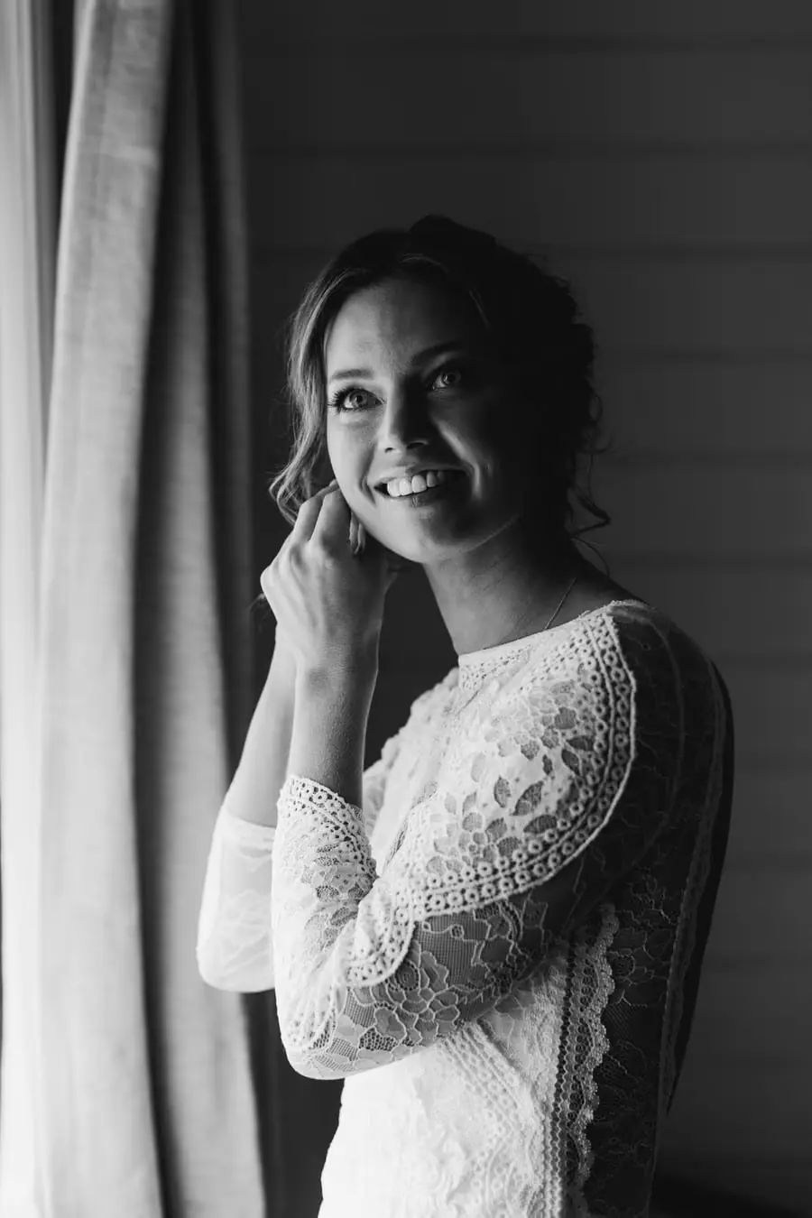 Black-and-white portrait of the smiling bride beside a window