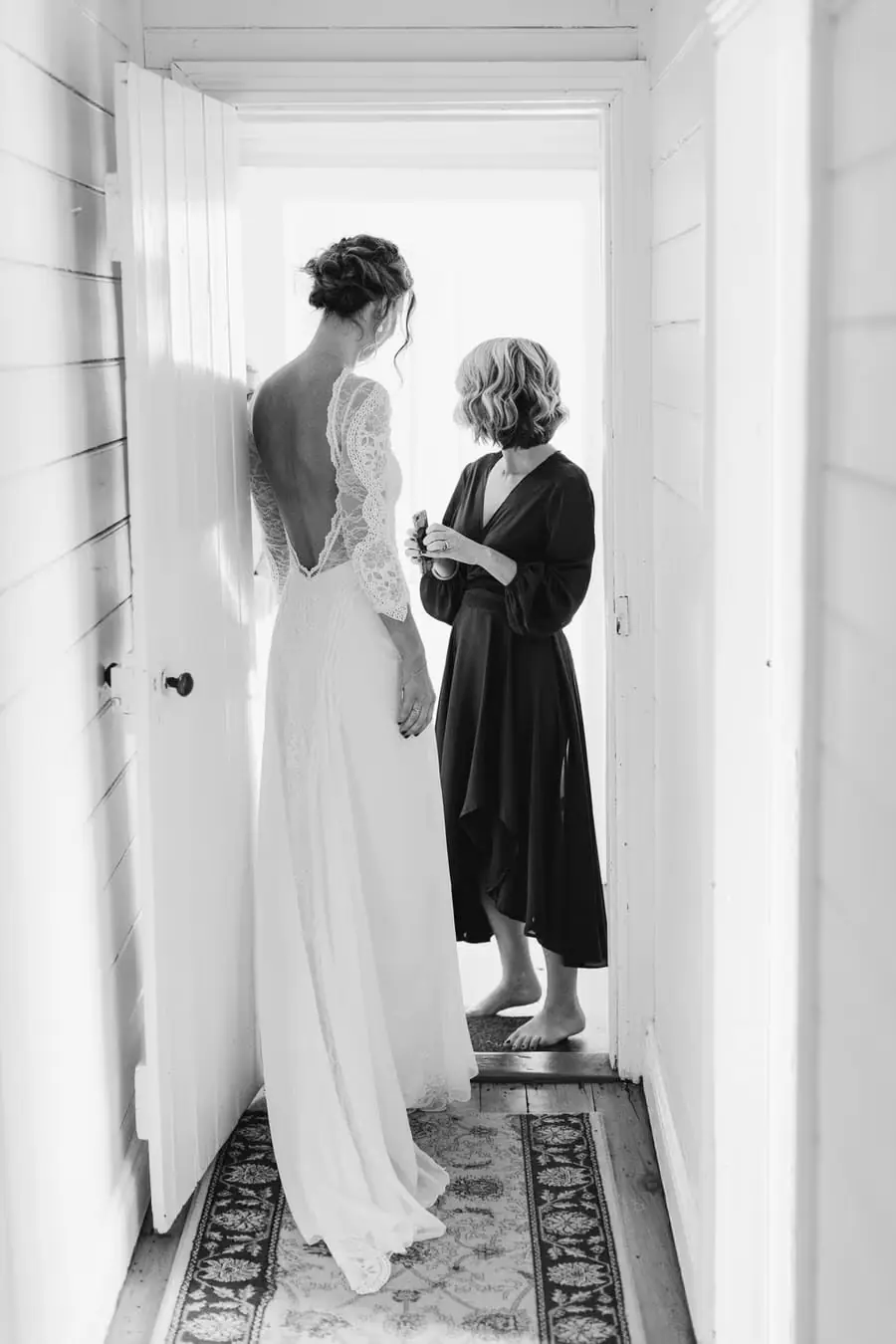 Black-and-white photograph of a woman helping the bride with her wedding dress