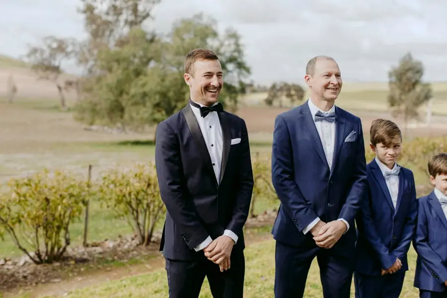 Groom smiling beside a man and boys wearing blue suits
