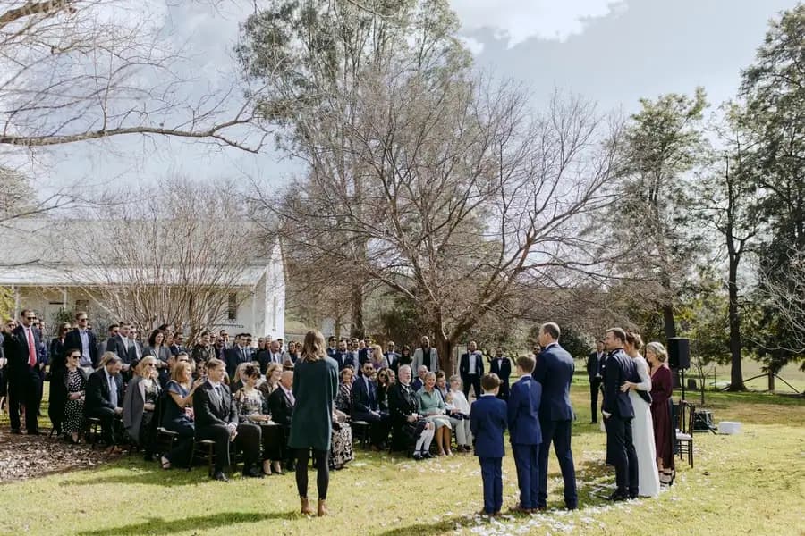 Outdoor ceremony beneath a bare tree with guests seated and green hills beyond