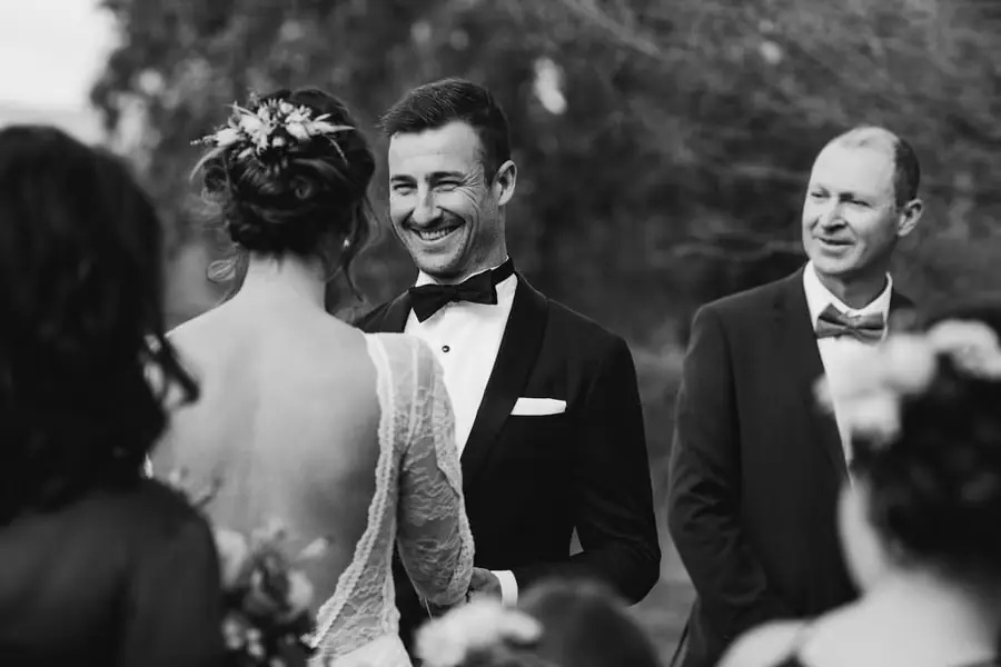 Black-and-white photograph of the groom smiling at the bride during their vows