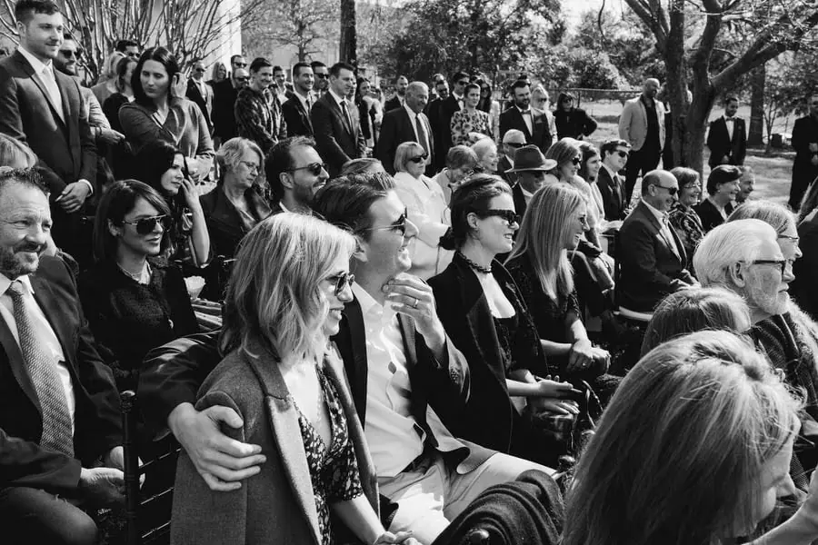 Black-and-white photograph of wedding guests smiling during the ceremony