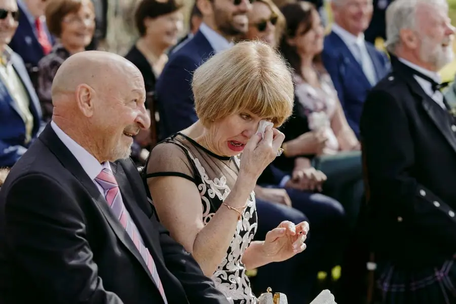 Seated wedding guest wiping her eye while the man beside her smiles
