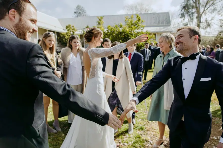 Bride extending an arm towards guests as the groom greets someone beside her