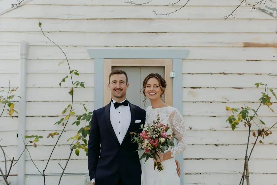 Bride and groom smiling in front of a weatherboard cottage