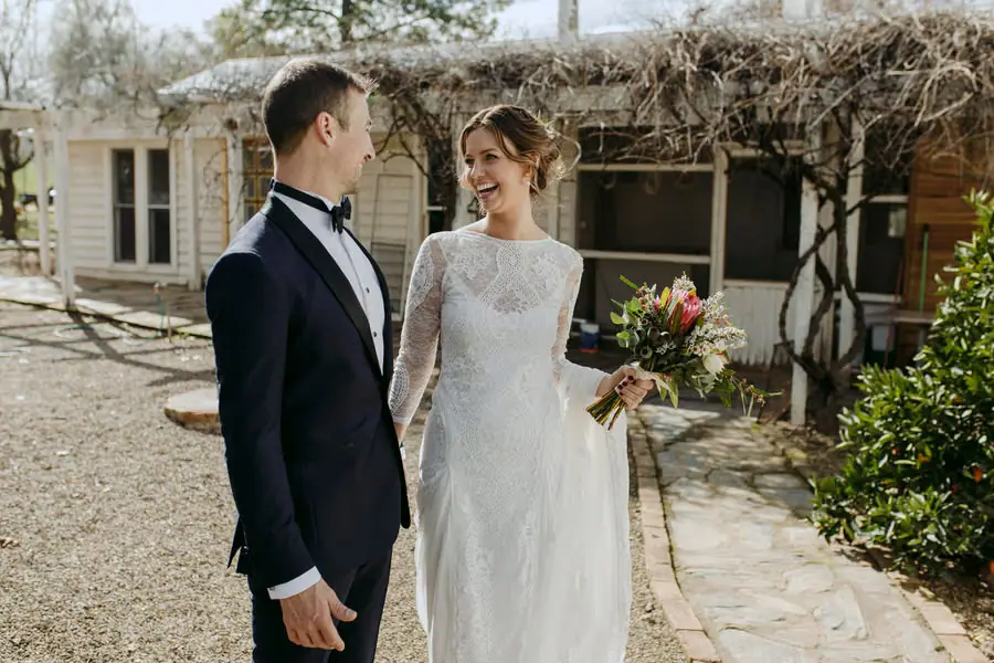 Bride and groom laughing together beneath bare vines beside the cottage
