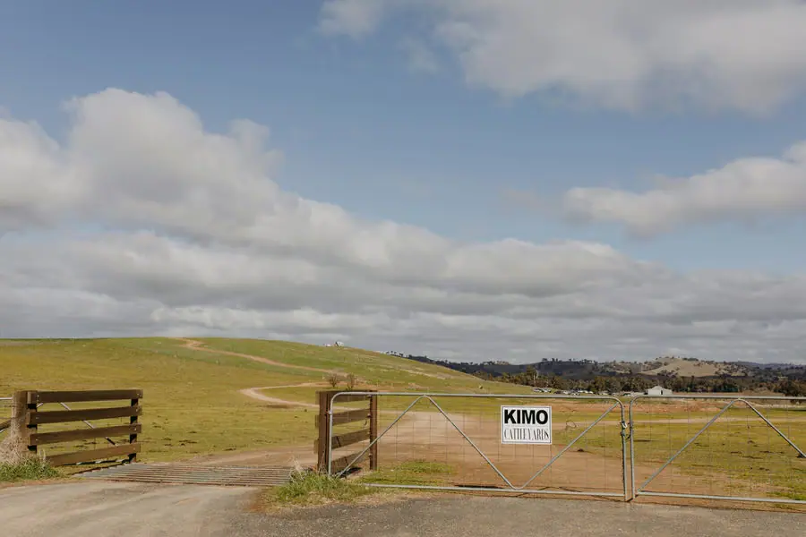 Farm gate and Kimo sign overlooking rolling farmland beneath scattered clouds