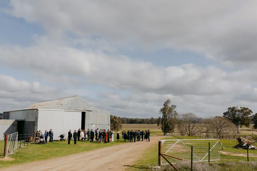 Guests gathered outside a metal-sided farm building beneath an open sky