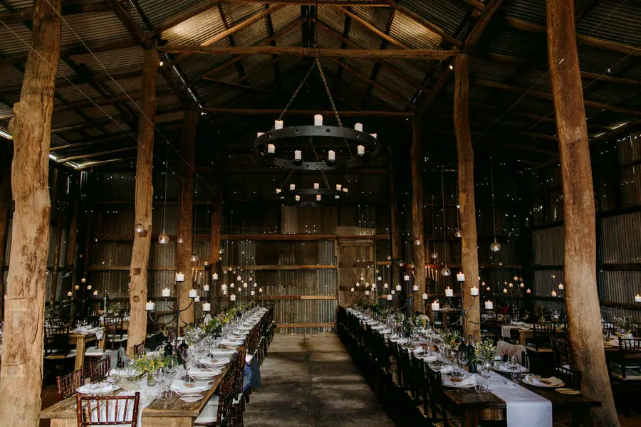 Long reception tables with candles beneath timber posts and roof beams