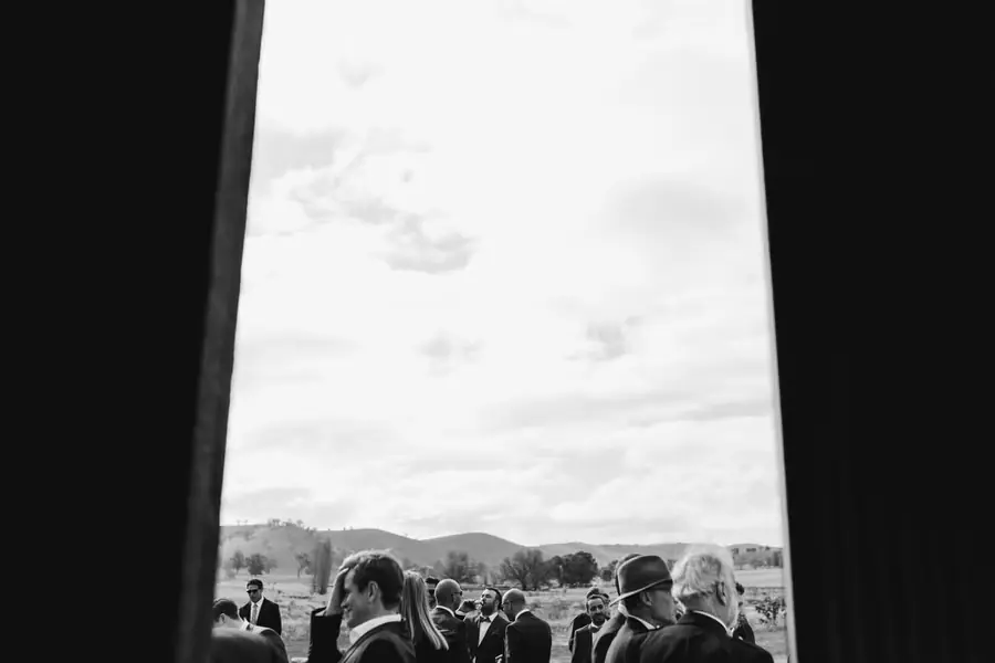 Black-and-white view through an open barn doorway towards guests and hills