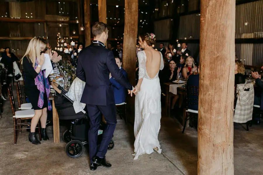 Bride and groom entering the reception holding hands as guests applaud
