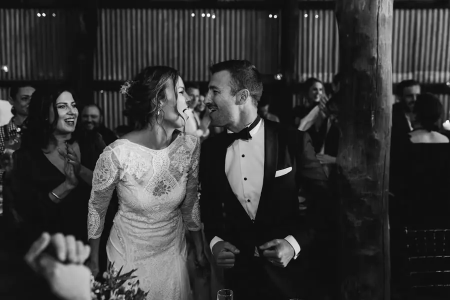 Black-and-white photograph of the bride and groom laughing among reception guests
