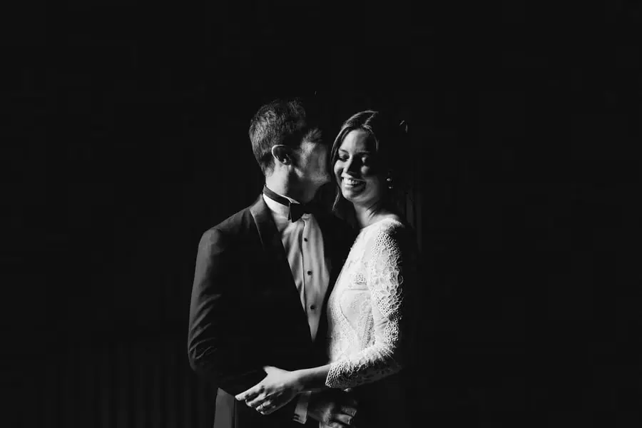 Black-and-white portrait of the bride and groom embracing against a dark background