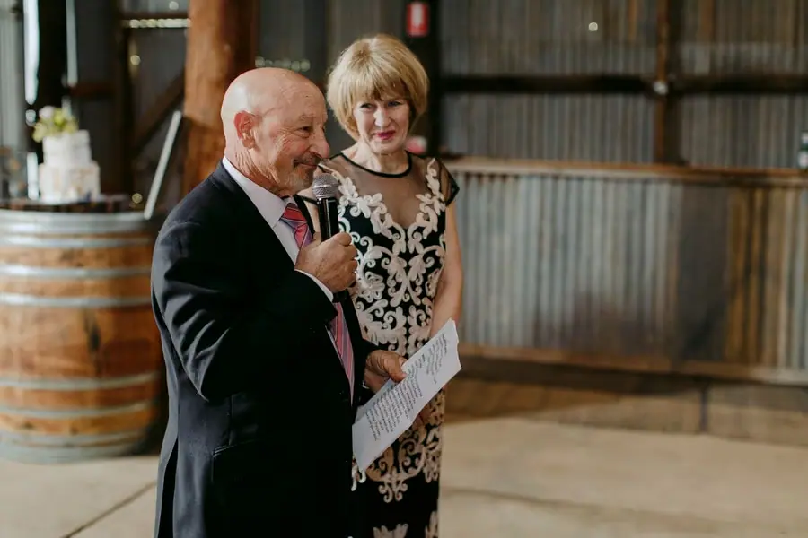 Man speaking into a microphone beside a woman holding notes at the reception