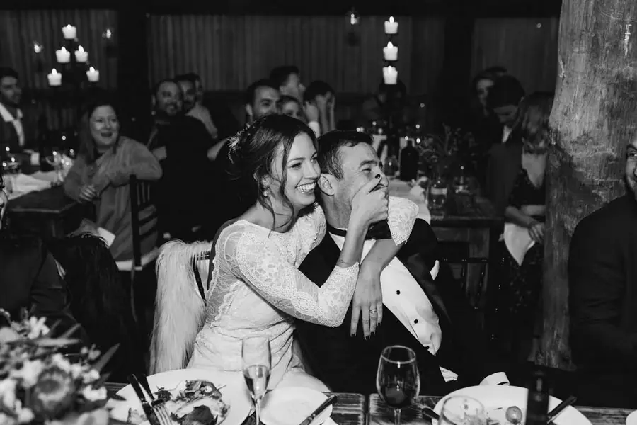 Black-and-white photograph of the seated bride cuddling the groom during the reception