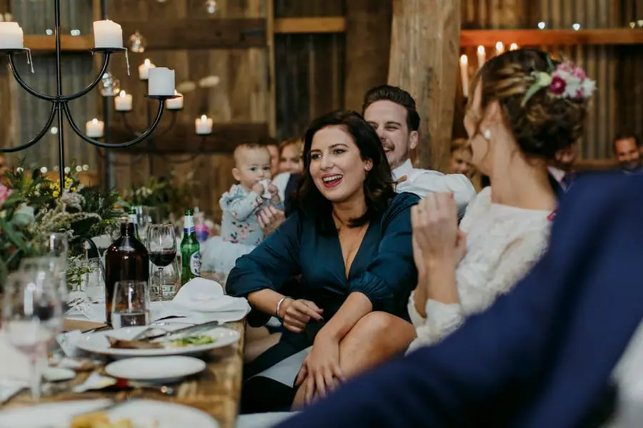 Bride and groom chatting with a smiling woman at a reception table