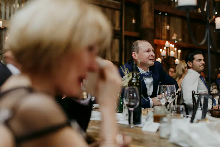 View past a seated woman towards men listening at a reception table