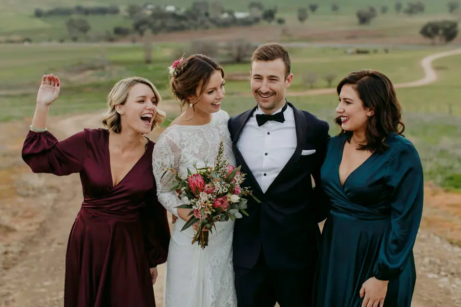 Couple laughing with two bridesmaids on a hillside above farmland