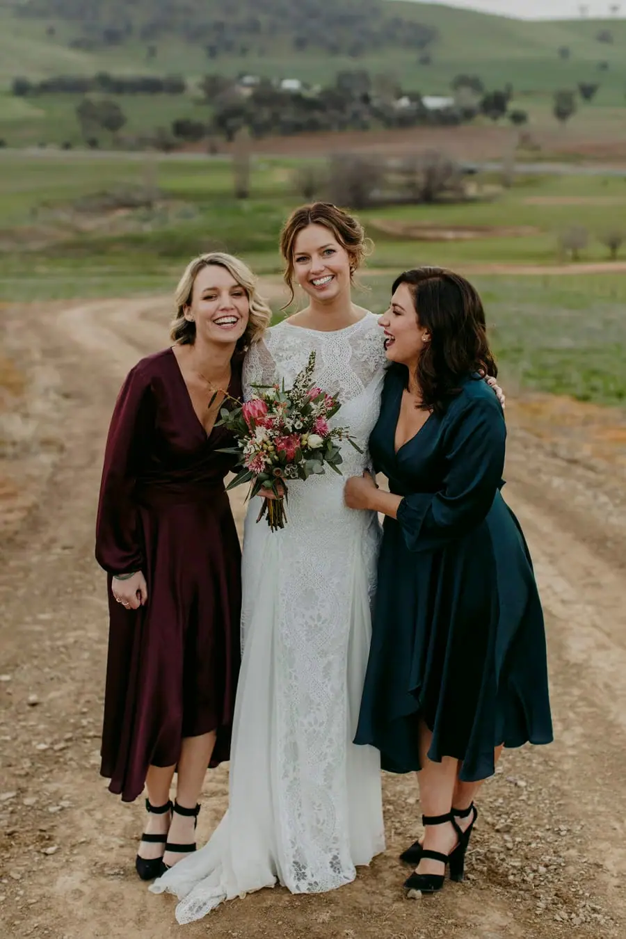Bride and two bridesmaids standing together with bouquets on a hillside