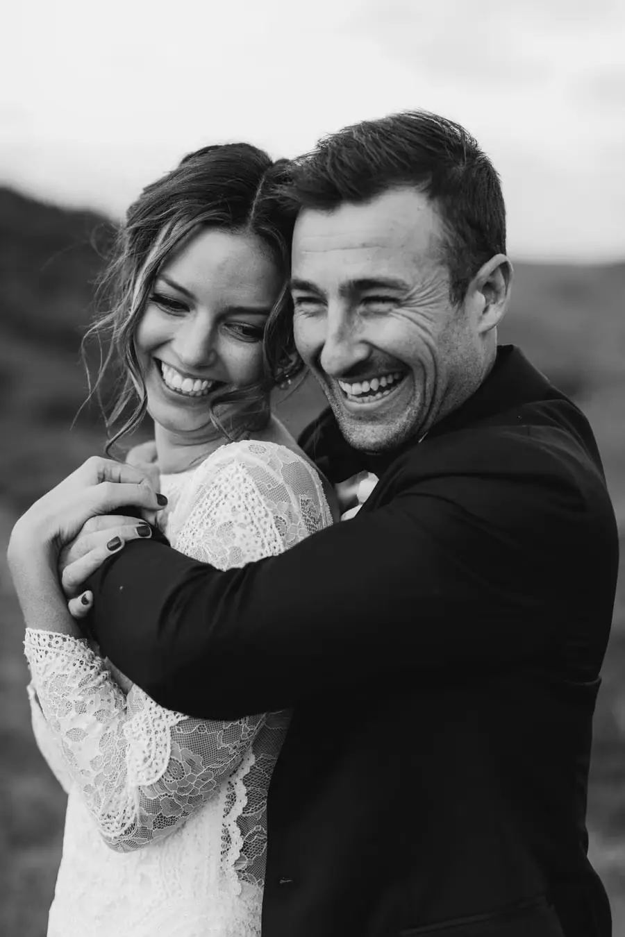 Black-and-white portrait of the couple laughing with their arms around each other