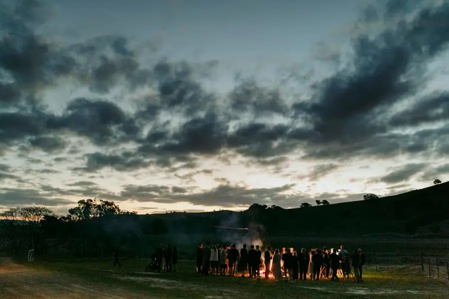 Guests gathered around an outdoor fire beneath a dramatic evening sky