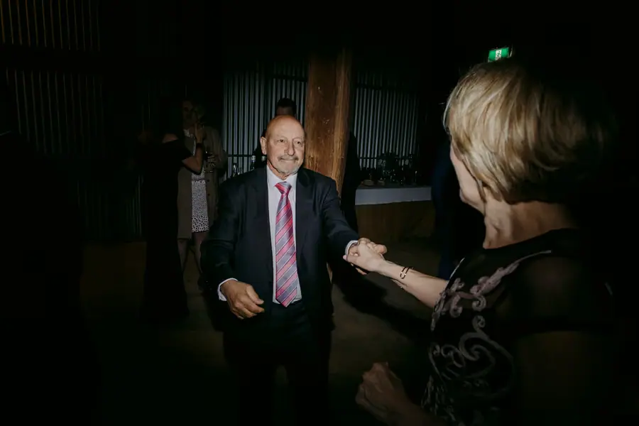 Man and woman holding hands and dancing in a dim reception room