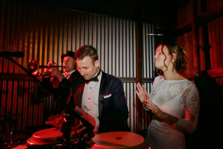 Groom playing the drums under red lights while the bride laughs beside him
