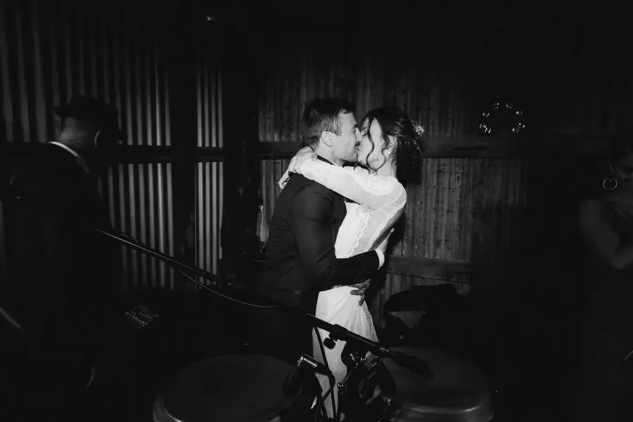 Black-and-white photograph of the bride and groom embracing and kissing beside the drums