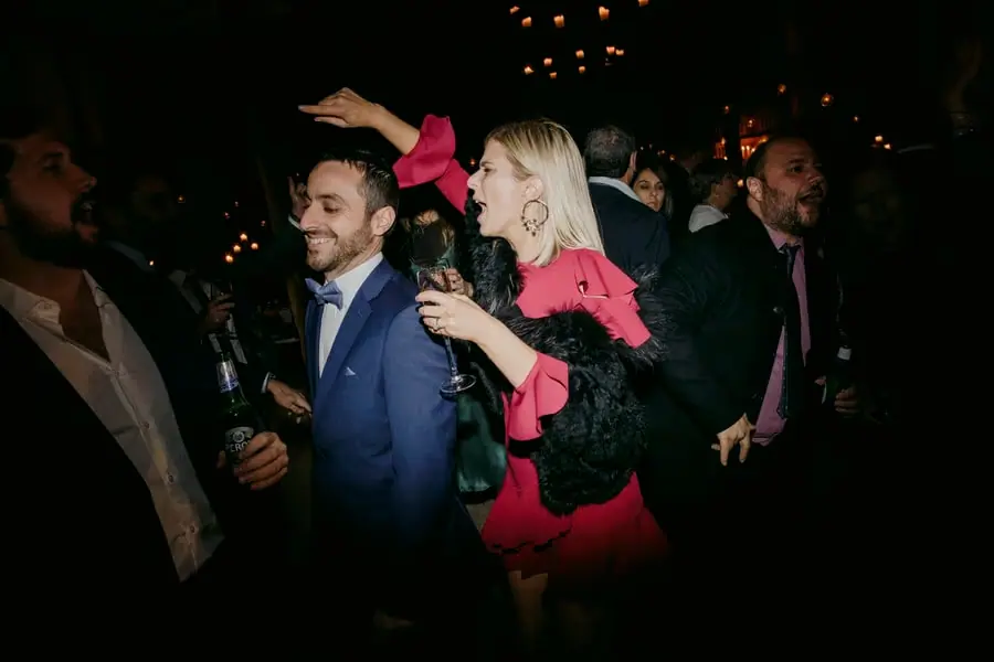 Woman in a pink dress dancing with an arm raised among wedding guests