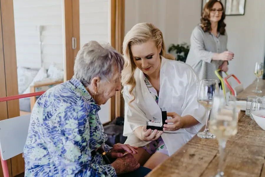 Bride showing a small gift box to an older woman beside champagne glasses