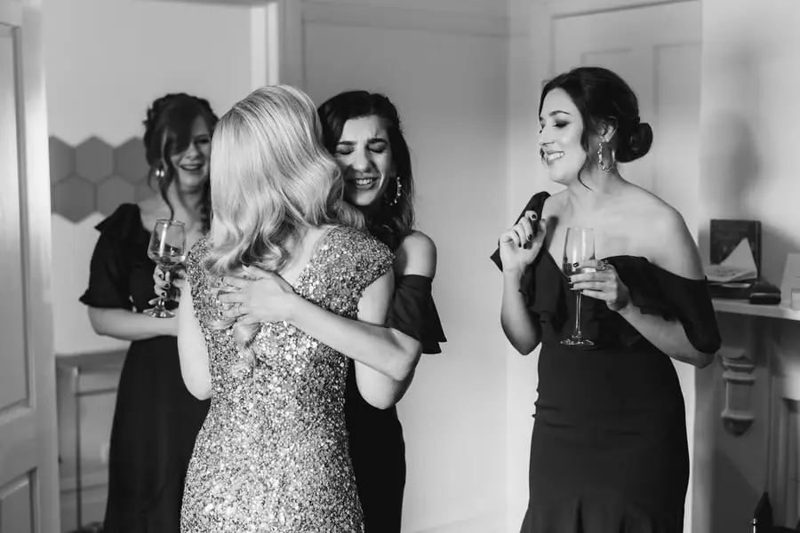 Black-and-white photograph of a bride embracing a friend while women smile nearby