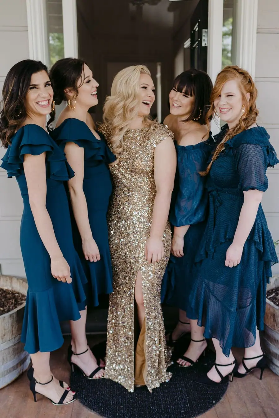 Bride in a gold dress posing with four friends in dark teal dresses