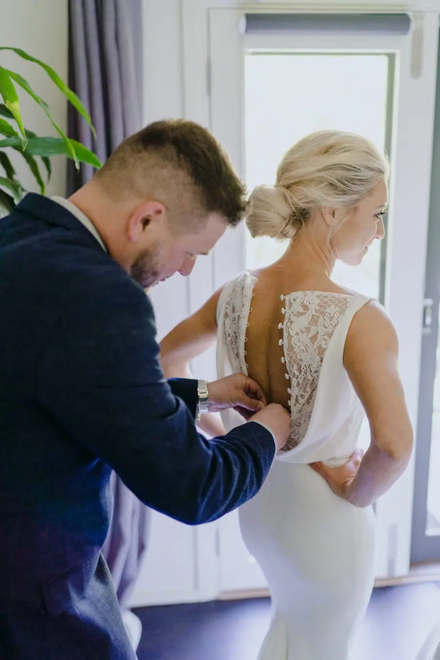 Friend fastening the lace back of a bride's white wedding dress